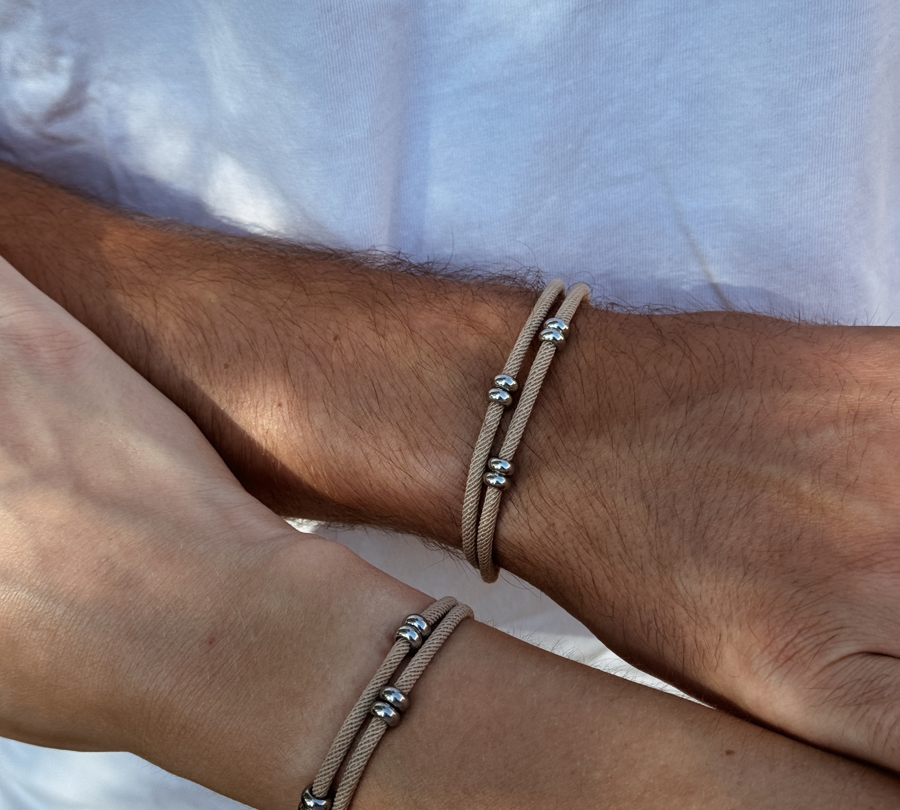 Deux poignets portant un bracelet commun couple discret mixte en acier inoxydable et cordon