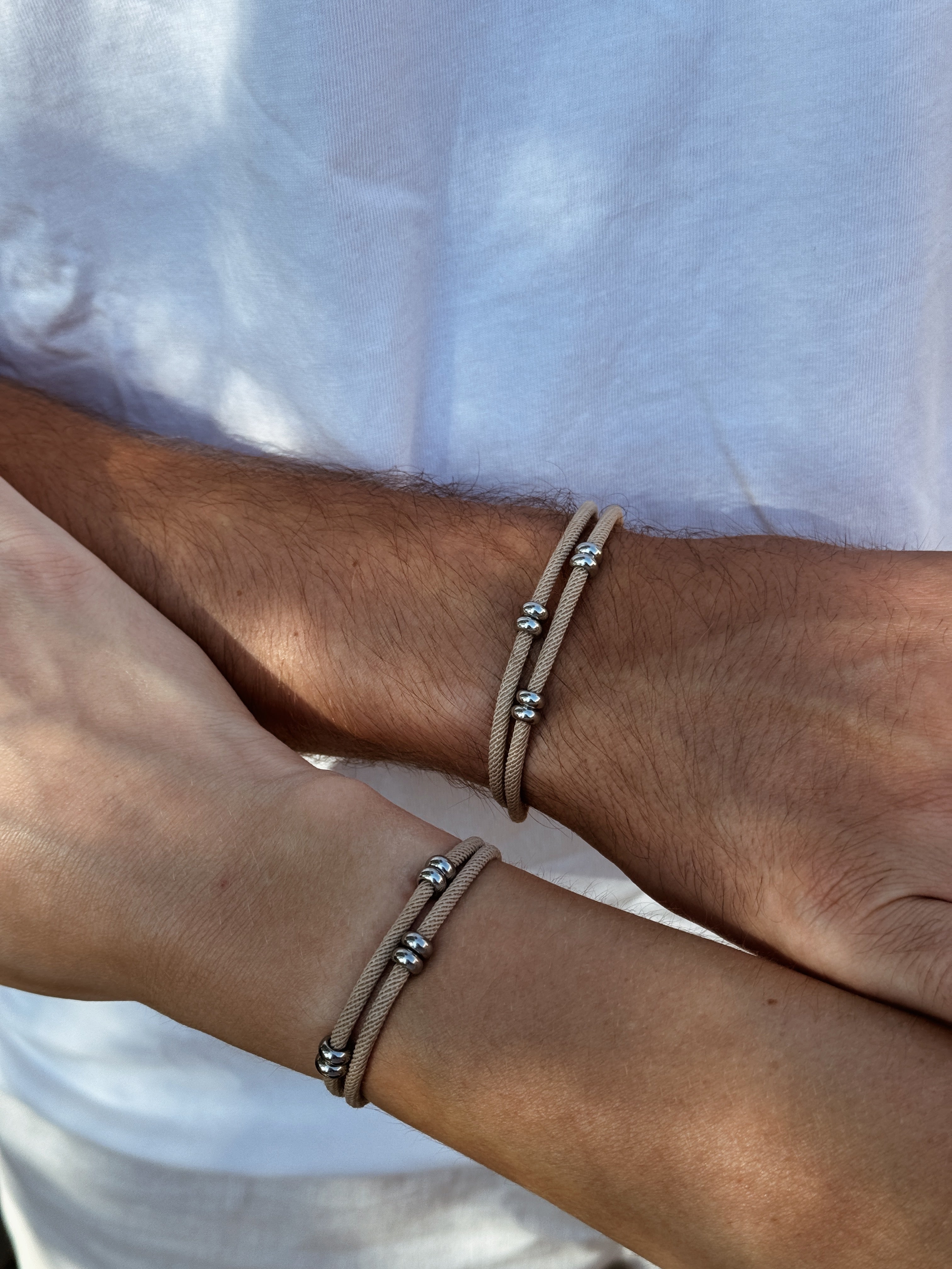 Deux poignets portant un bracelet commun couple discret mixte en acier inoxydable et cordon